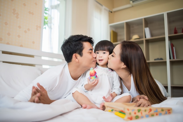 家庭のベッドで遊んでいる両親と幸せな子供