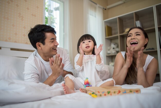 家庭のベッドで遊んでいる両親と幸せな子供