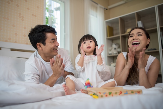 家庭のベッドで遊んでいる両親と幸せな子供