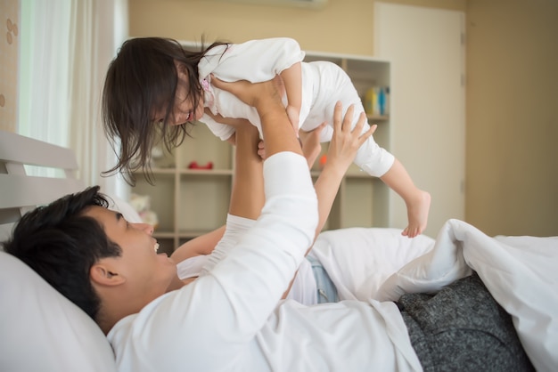 家庭のベッドで遊んでいる両親と幸せな子供