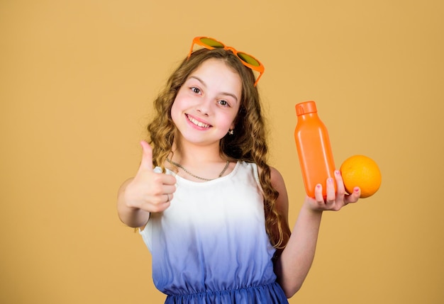 幸せな子供時代。天然ビタミン源。子供の女の子はオレンジ色の果物を食べ、オレンジジュースを飲みます。ビタミンの栄養。ファッションキッズサングラスはさわやかなビタミンジュースを飲みます。健康管理。夏のビタミンダイエット。