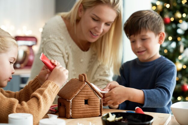Счастливые дети украшают пряничный домик со своей мамой