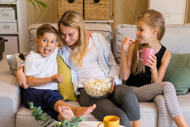 Счастливые дети и ее мать едят попкорн