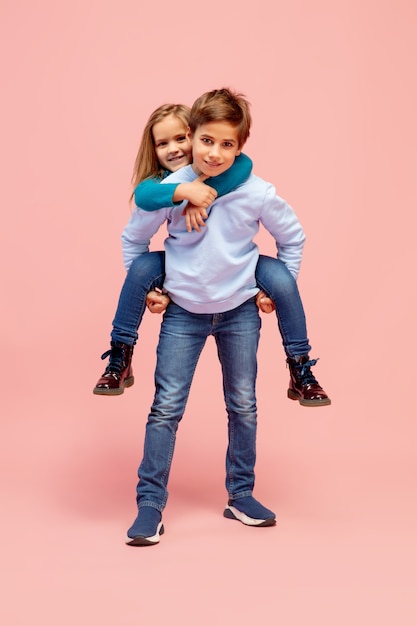 Happy children isolated on coral pink studio background. Looks happy, cheerful, sincere. Copyspace. Childhood, education, emotions concept