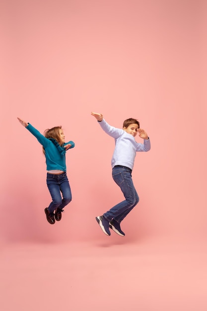 珊瑚ピンクのスタジオの背景に分離された幸せな子供たち。幸せで、陽気で、誠実に見えます。コピースペース。幼児期、教育、感情の概念 Premium写真