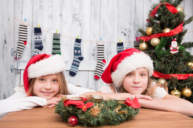 산타 모자를 쓴 행복한 아이들은 테이블에 누워 새해와 크리스마스 축하를 기다리고 카메라를 바라보고 있습니다.
