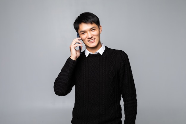 Happy Chinese man using a smartphone isolated against white wall.