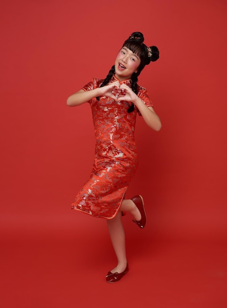 Happy Chinese new year children asian girl wearing traditional qipao dress with gesture mini heart