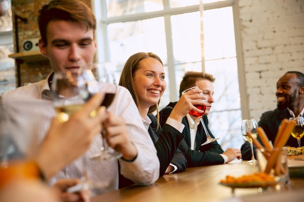 Happy co-workers celebrating while company party, corporate event. Young caucasian people in business attire talking, drinking wine.