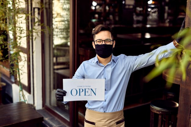 Happy coffee shop owner holding open sign while reopening after coronavirus pandemic