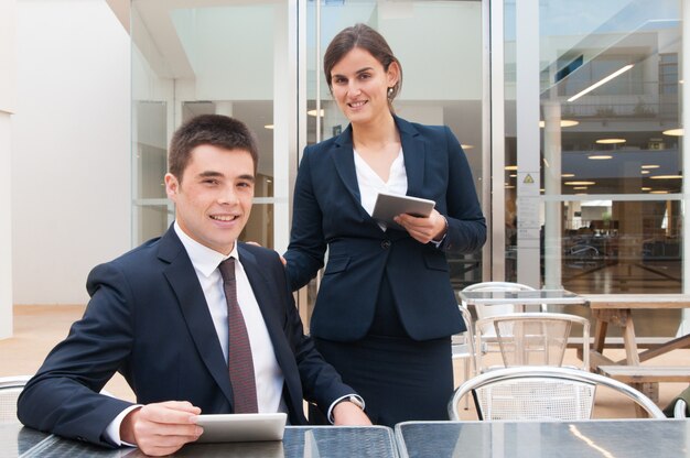 Happy colleagues holding tablets and posing at camera