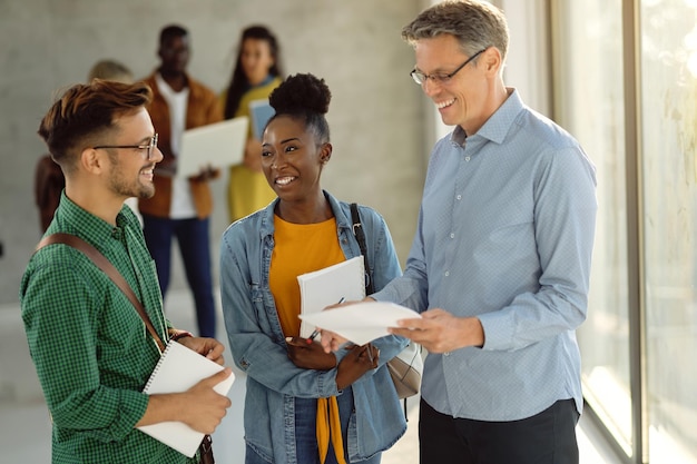 Happy college students communicating with their professor in a hallway