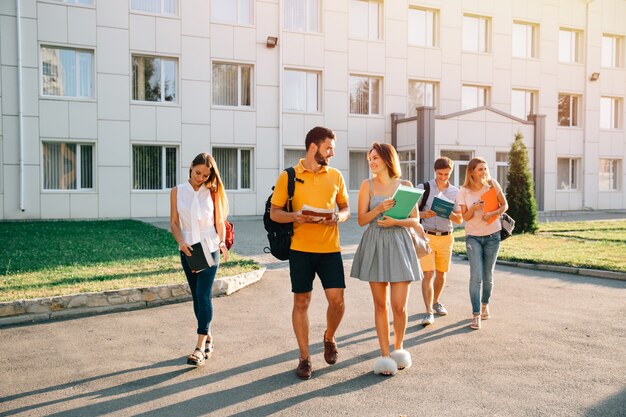 Happy college students with books in hands walking together on campus