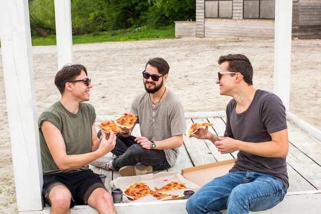 Happy company chatting and eating pizza on picnic