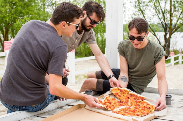 Счастливая компания с пиццей отдыхает на природе