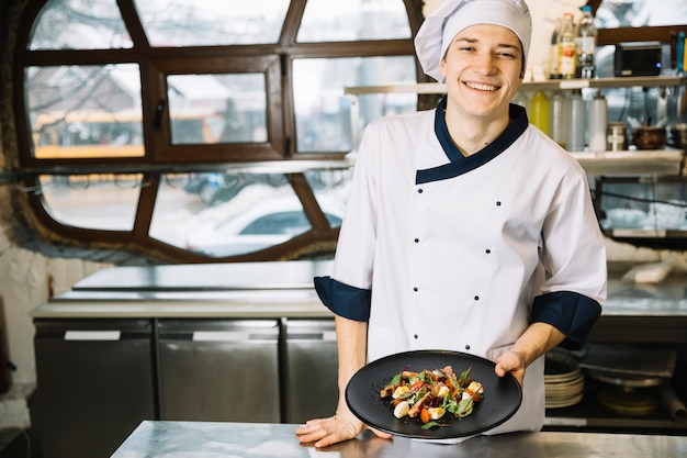 Free photo happy cook holding salad with meat on plate