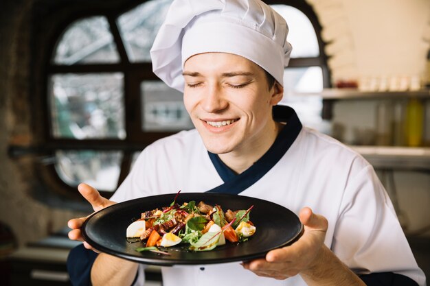 Happy cook smelling salad with meat on plate