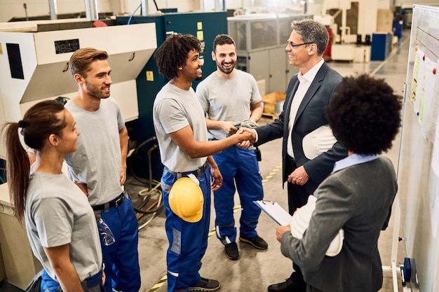 Free photo happy corporate manager shaking hands with black worker after staff meeting in a factory