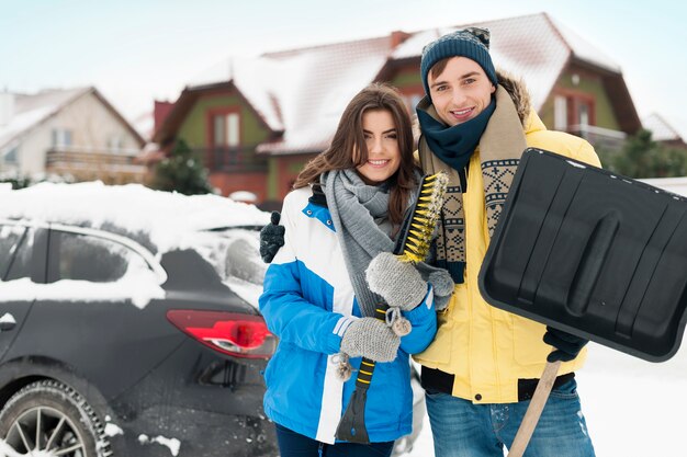 Happy couple are ready to cleaning car from snow