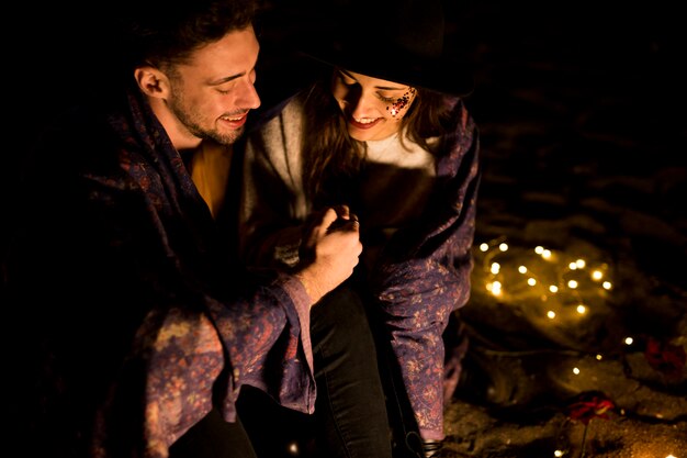 Happy couple in blanket holding hands on sea shore