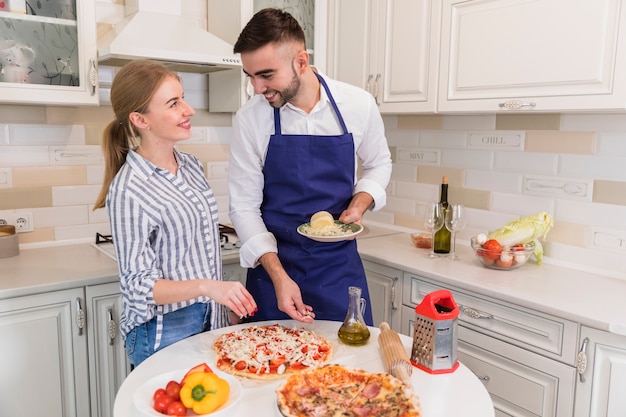 Happy couple cooking pizza with cheese in kitchen