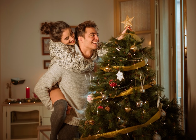 Free photo happy couple decorating christmas tree with star