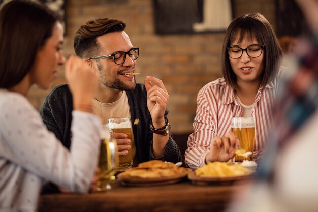 Happy couple drinking beer and eating tortilla chips with friends in a pub