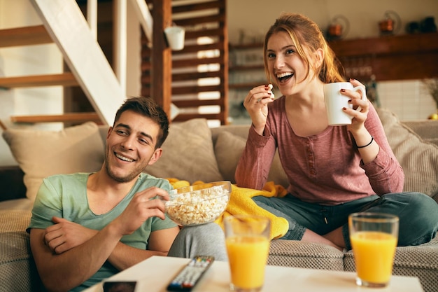 Happy couple eating popcorn while watching movie at home