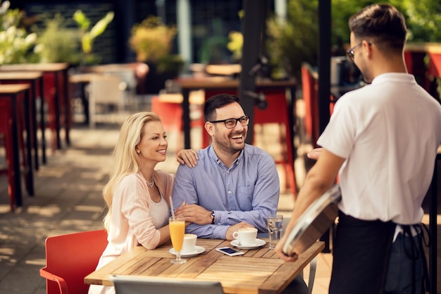 Happy couple enjoying in a cafe while talking to a waiter