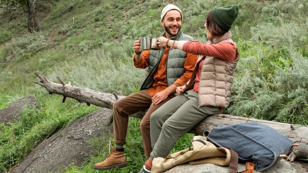 Happy couple enjoying hot drink sitting on log