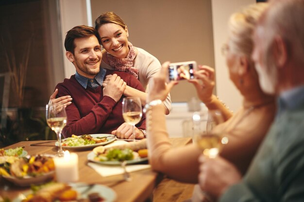 ダイニングルームでの家族の食事中に写真を撮られている間楽しんで幸せなカップル