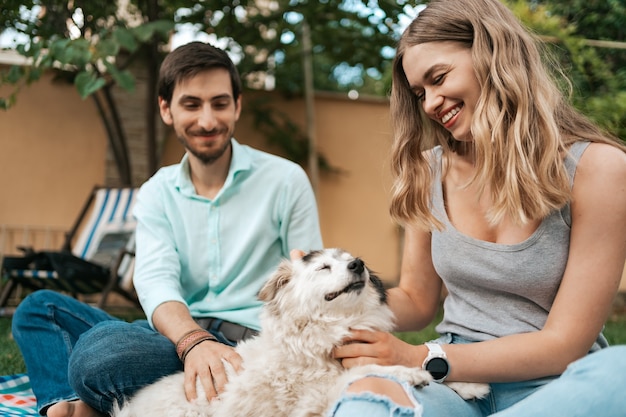 草の上の裏庭で犬と遊んでいる男の幸せなカップル。元気な老犬