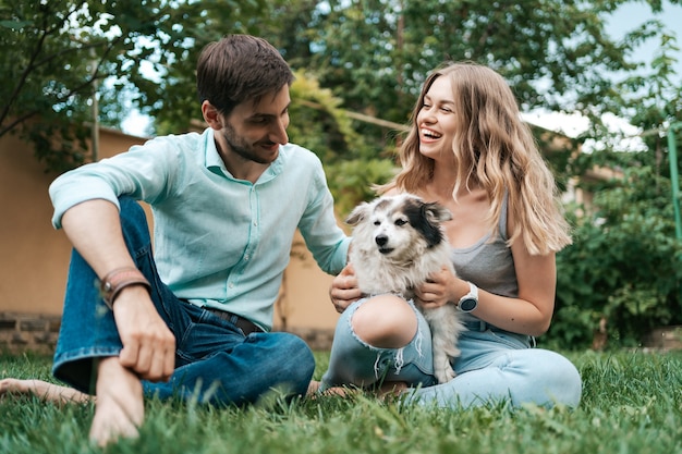 Happy couple of guys playing with their dog in the backyard on the grass. Cheerful old dog