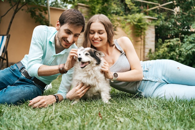 Happy couple of guys playing with their dog in the backyard on the grass. Cheerful old dog