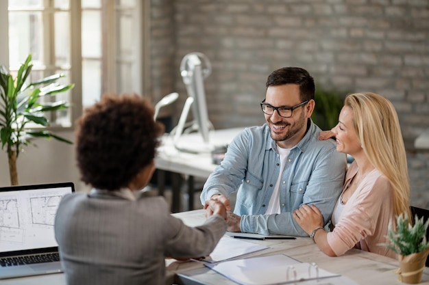 happy couple handshaking with financial advisor on a meeting in the office focus is on man