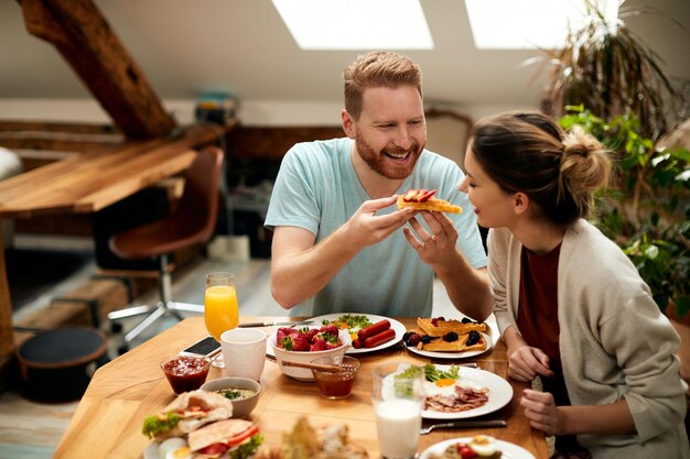 ダイニングテーブルで朝食にワッフルを食べながら楽しんで幸せなカップル