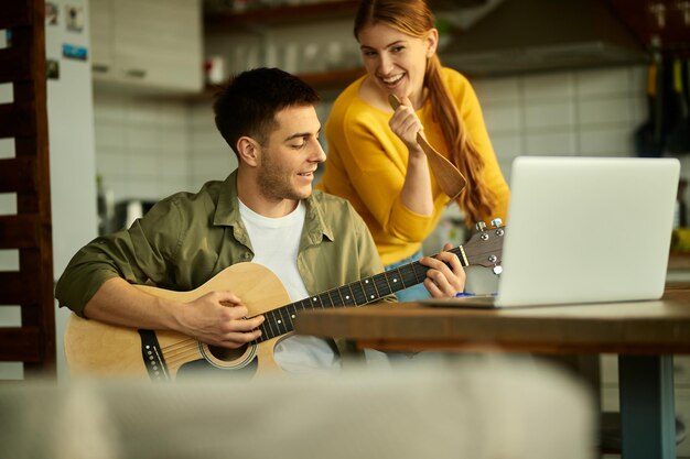 Счастливая пара веселится, играя на акустической гитаре и поя дома