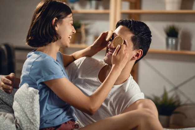 食べ物を楽しんでいる幸せなカップル若い女性はクッキーを保持し、彼氏の目を覆っています