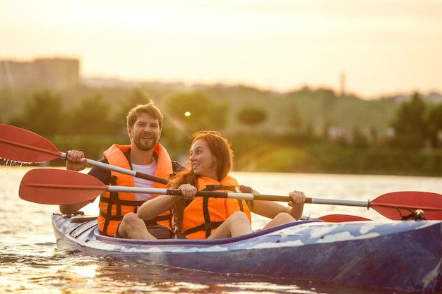 Happy couple kayaking on river with sunset on the background