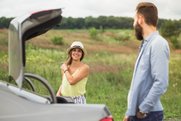 開いているトランクで車の近くに立っているお互いを見ている幸せなカップル