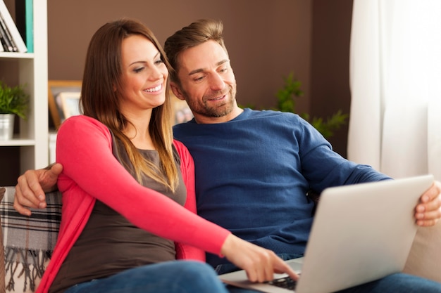 Счастливая пара, глядя на экран ноутбука на диване у себя дома
