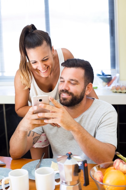 Happy couple looking at mobile phone screen at breakfast