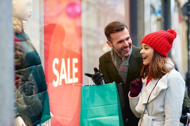 Happy couple looking at shop window with clothing