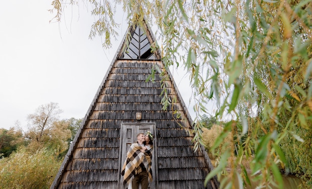 Счастливая влюбленная пара целуется перед сказочным деревянным домом посреди парка