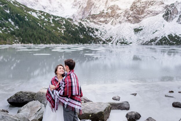 Happy couple in love is looking on each other in front of breathtaking winter mountain scenery and frozen lake, Tatry mountains