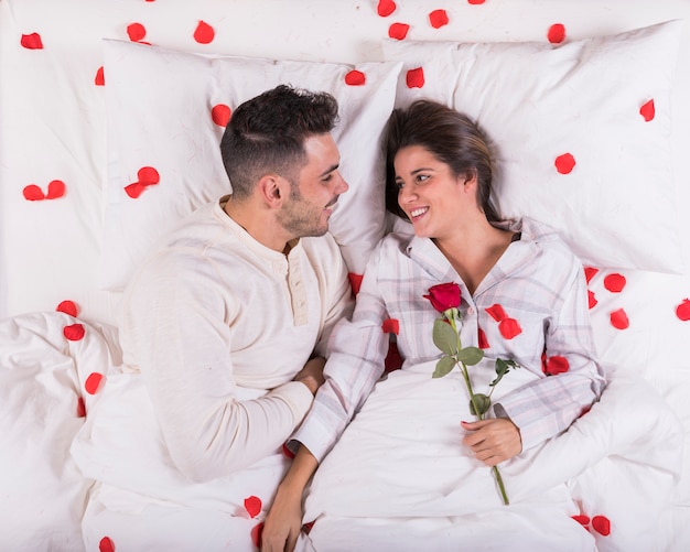 Happy couple lying in bed with rose 