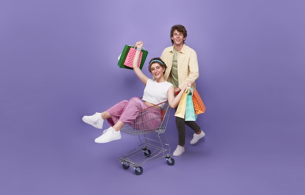 Happy couple lying in shopping cart and hand holding shopping bag rushing next shop store