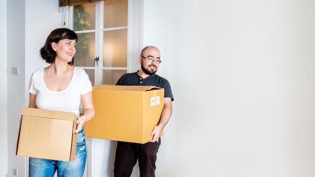 Happy couple moving in together and carrying boxes design space