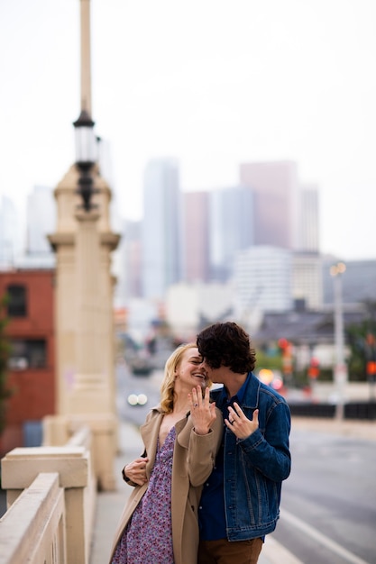 Happy couple posing outdoors in the city with engagement ring