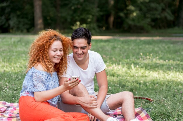 幸せなカップルはリラックスして公園で携帯電話をチェック